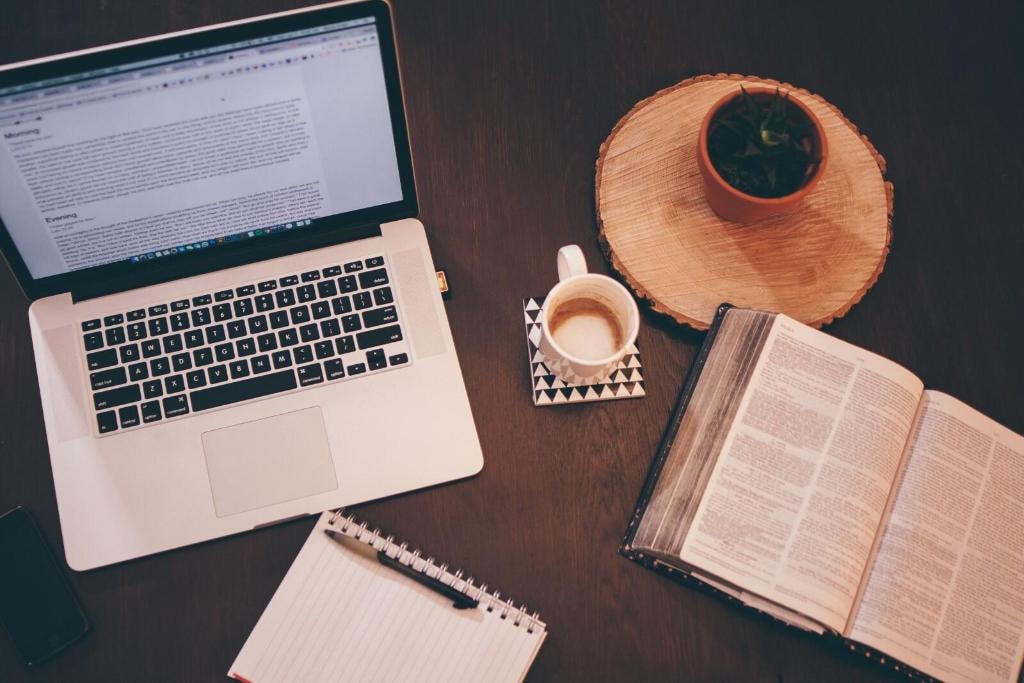 Laptop, coffee, and open Bible on a wooden desk